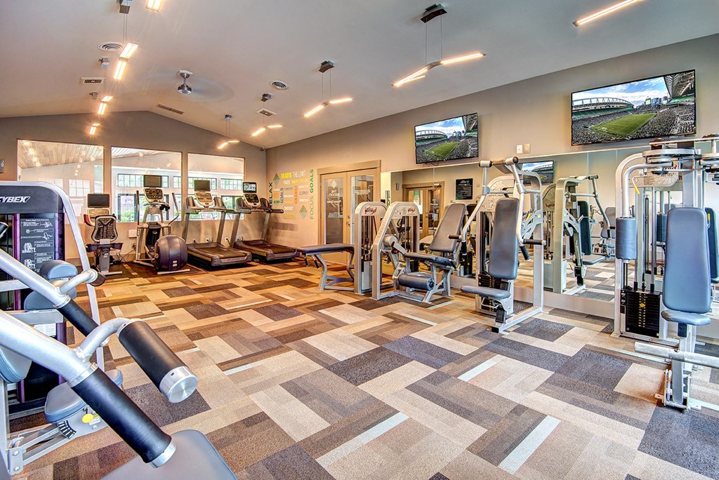 a spacious fitness center with cardio equipment and flat screen tvs
