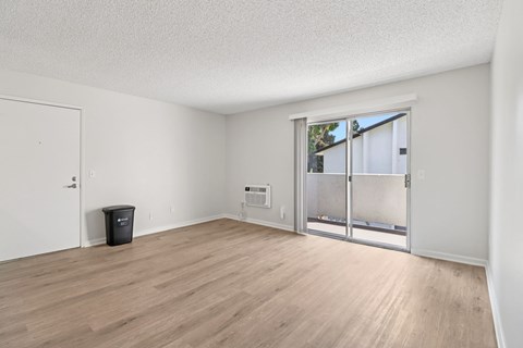A room with a white door, a window with a view of trees outside, and a black trash bin on the floor.