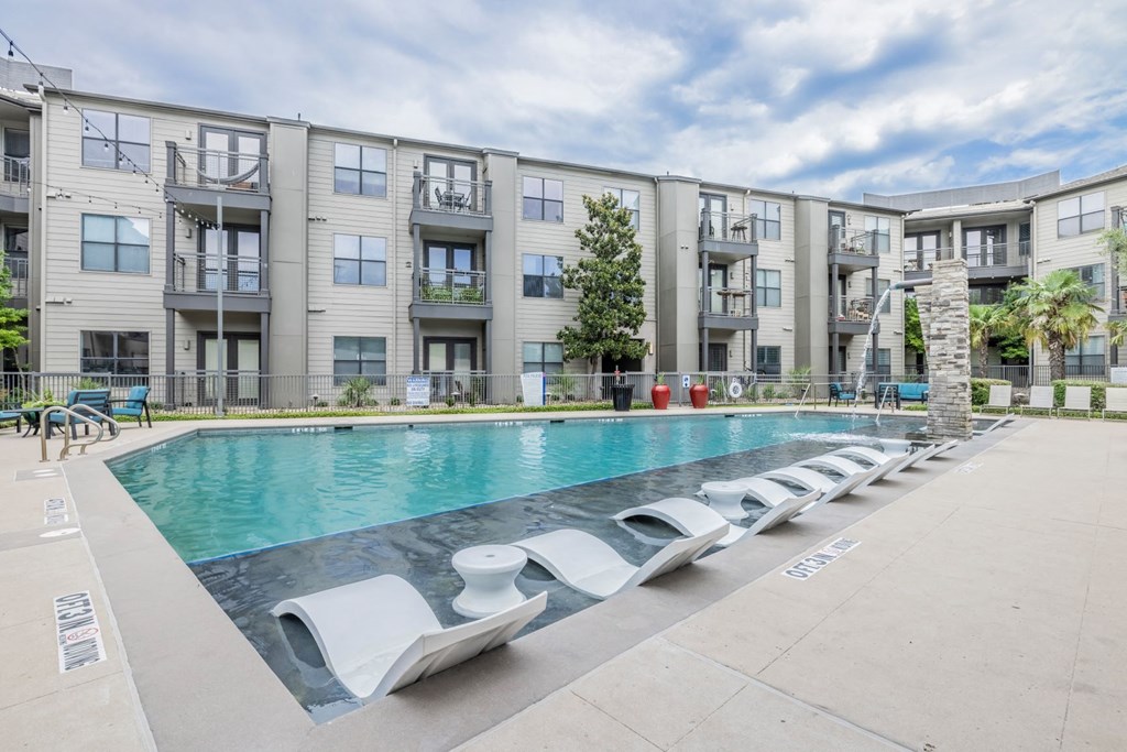 a swimming pool with chaise lounge chairs in front of an apartment building