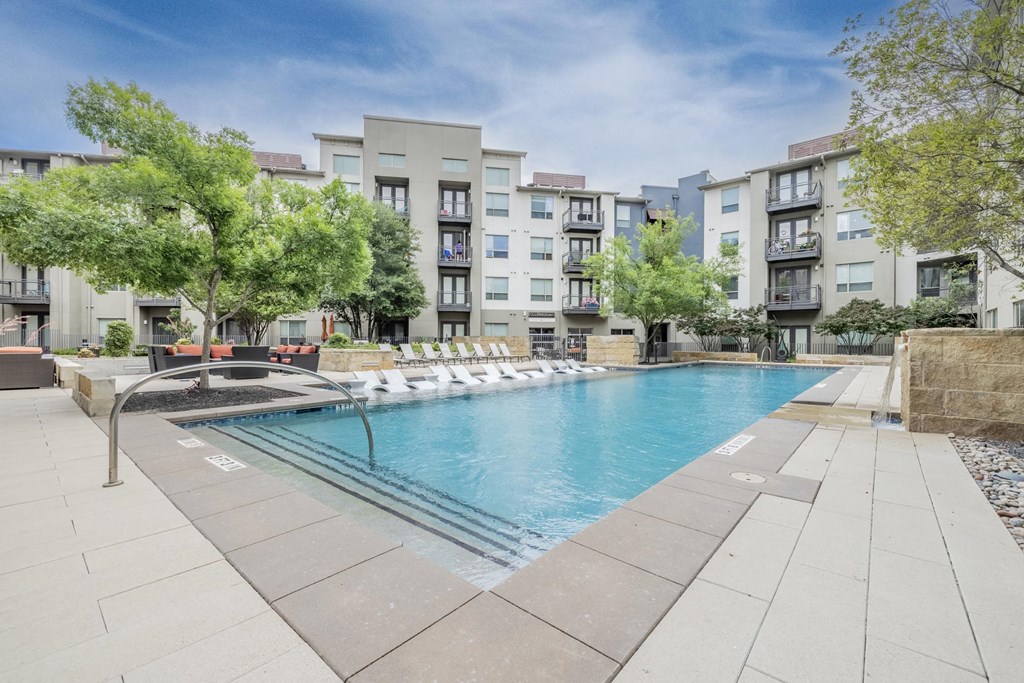 a swimming pool with chaise lounge chairs and trees in front of an apartment building