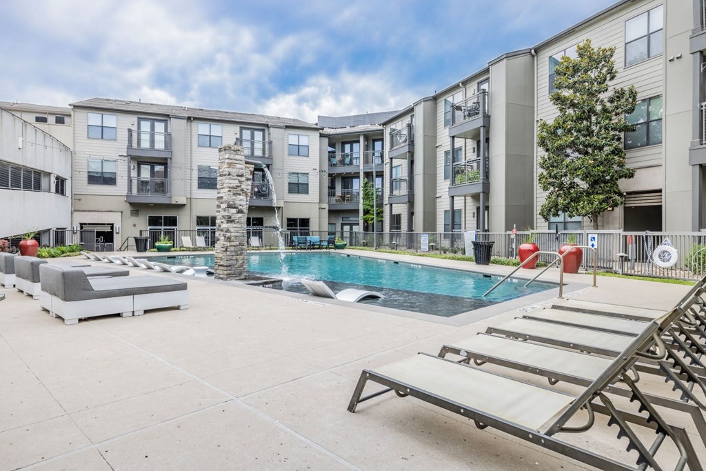 a swimming pool with chaise lounge chairs and a stone fireplace in front of an apartment building