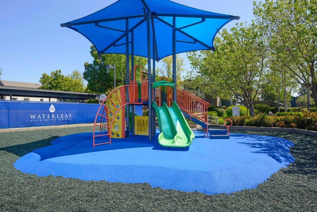 a playground with a blue umbrella and red and yellow slides