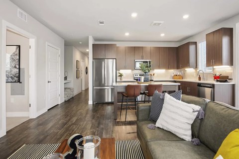 A modern kitchen and living room with a grey couch and wooden floors.