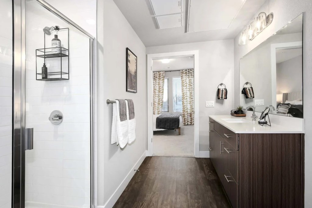 A bathroom with a white tile shower, a wooden vanity, and a large mirror.