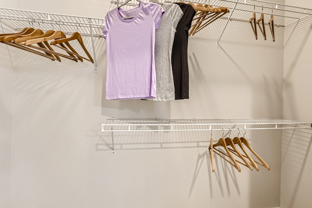 a walk in closet with a white clothes rail and a white closet organizer with gold hangers