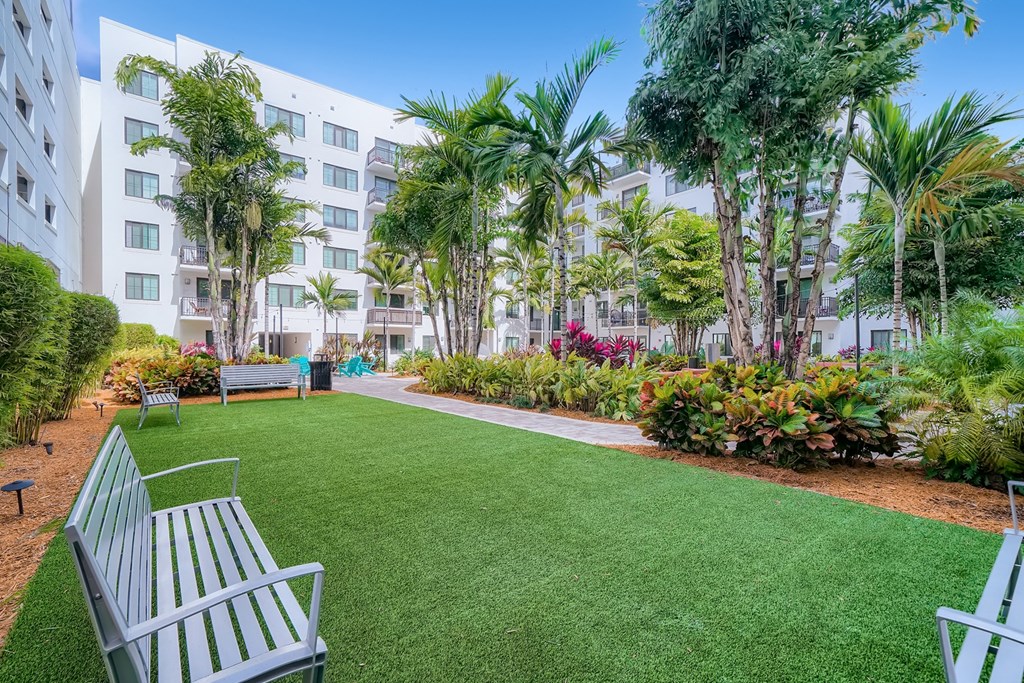 a garden with a lawn and benches in front of an apartment building
