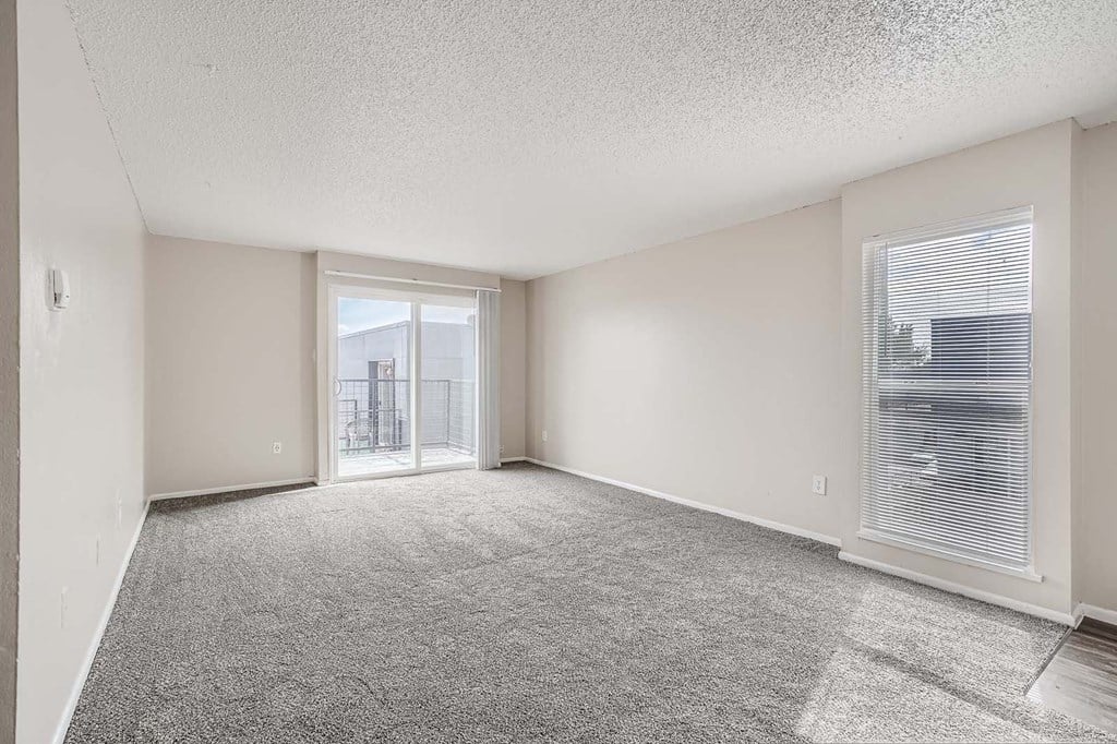 an empty living room with a sliding glass door to a balcony