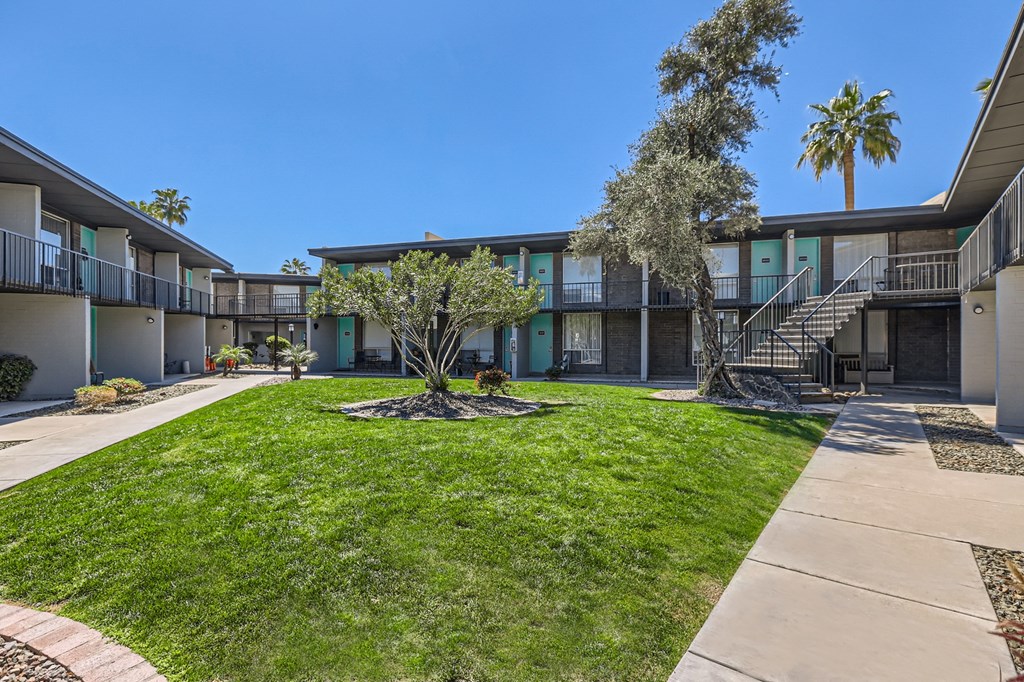 a courtyard with green grass and a building with stairs and palm trees