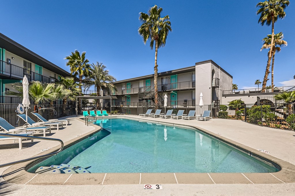 a swimming pool with chairs and palm trees in front of a building