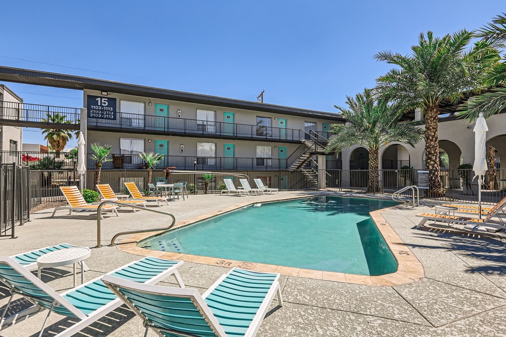 a pool with chairs and palm trees in front of a hotel