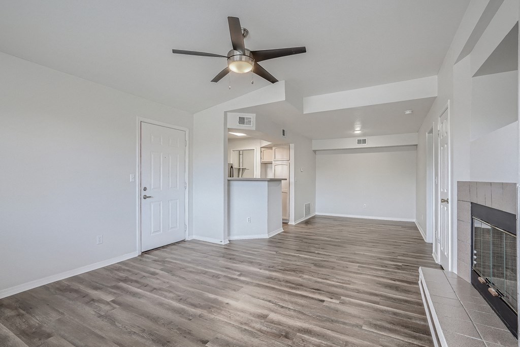 an empty living room with a ceiling fan and a kitchen