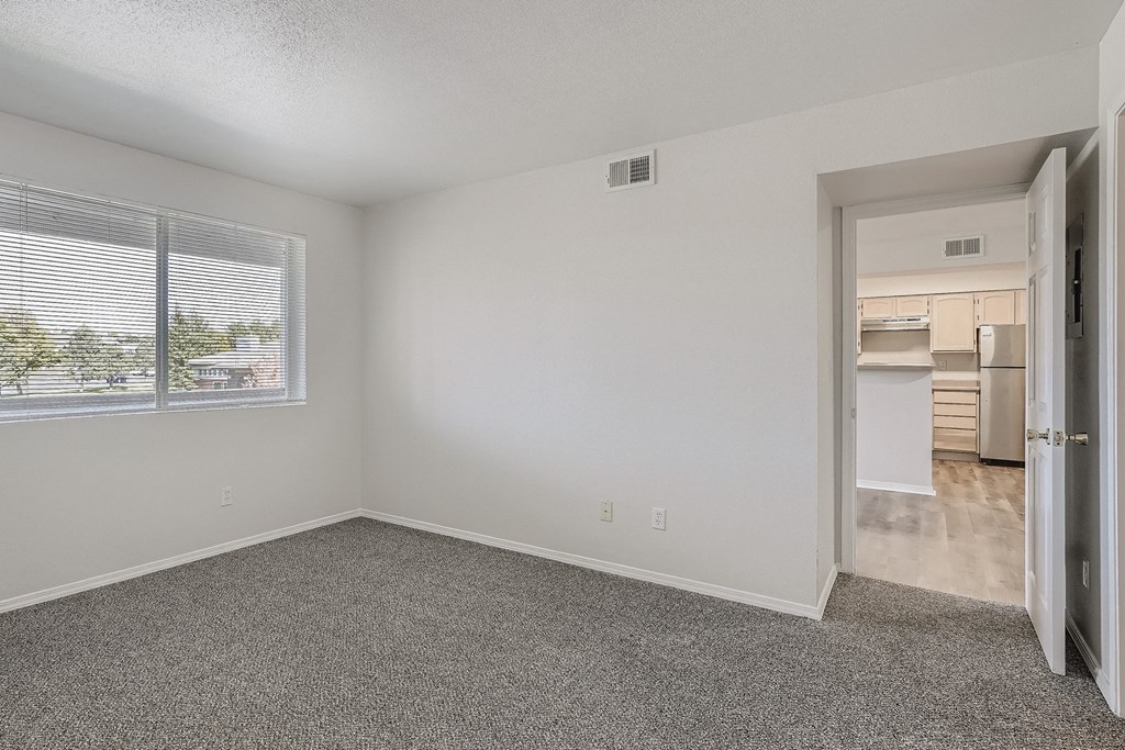 an empty room with a window and a door to a kitchen