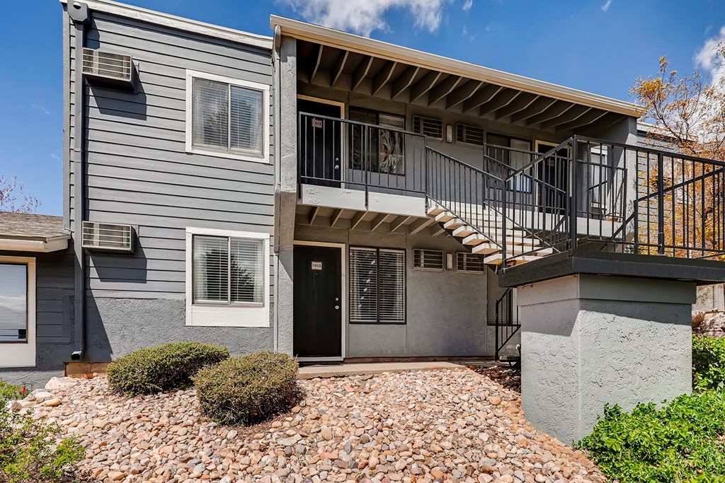 a gray house with a balcony and a gravel driveway