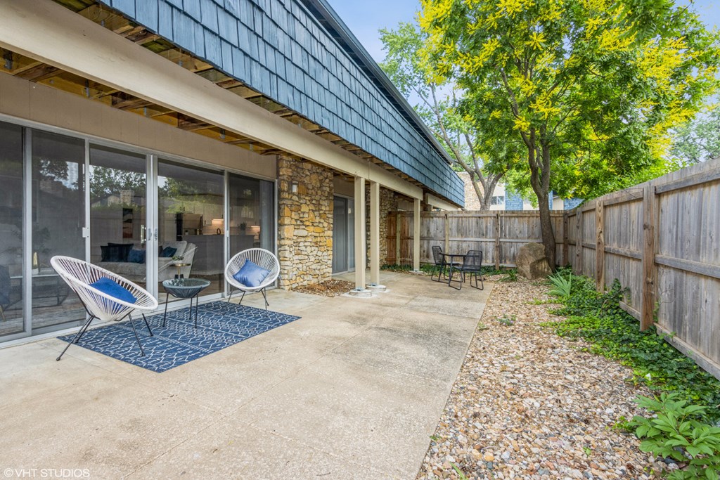 a patio outside a house with chairs and a tree