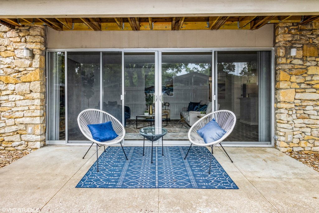 a patio with two chairs and a rug in front of sliding glass doors