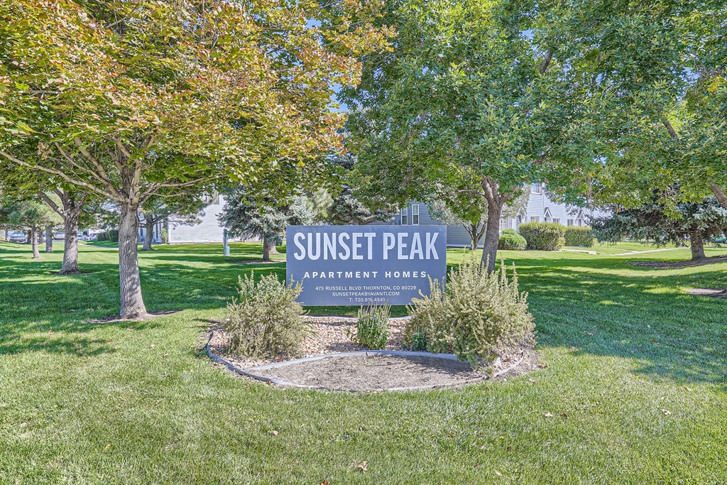 a park with trees and grass and a sign that says sunset peak apartments