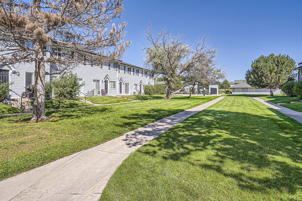 a sidewalk leads through a grassy area with trees and buildings in the background