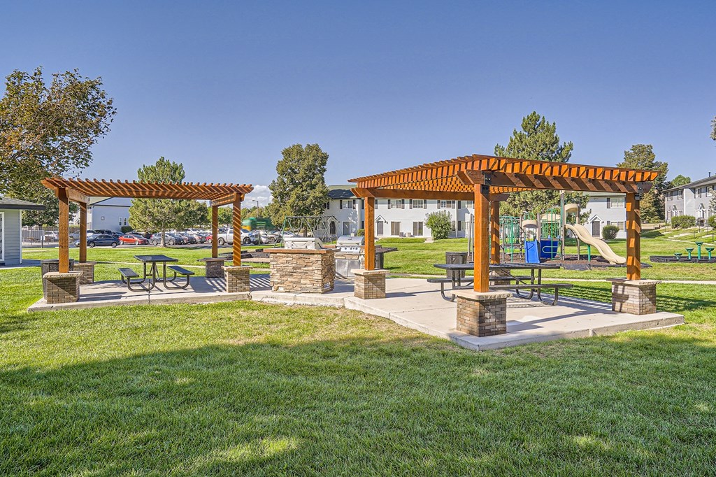 a picnic area with benches and a pergola in the middle of a grassy area
