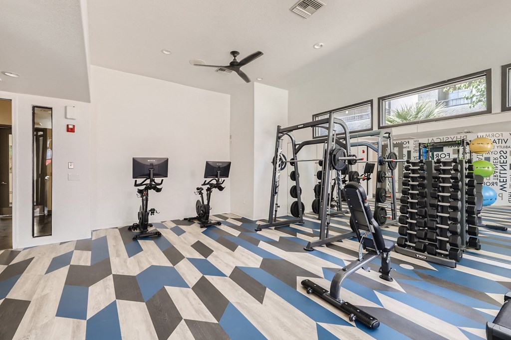 a gym with weights and cardio machines and a ceiling fan