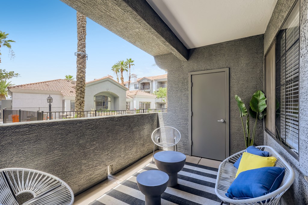 a patio with two chairs and a table and a wall with palm trees