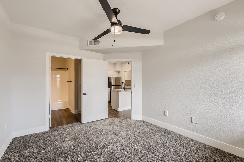 an empty living room with a ceiling fan and a kitchen