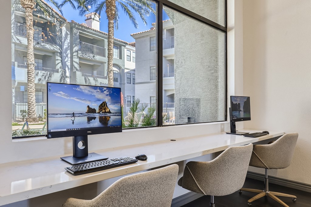 two computer monitors sitting on a desk in front of a window
