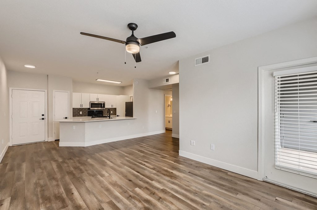 an empty living room with a ceiling fan and a kitchen