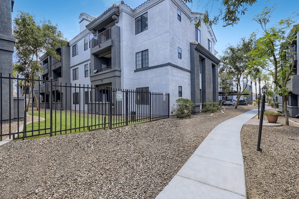 an apartment building with a sidewalk and a fence in front of it