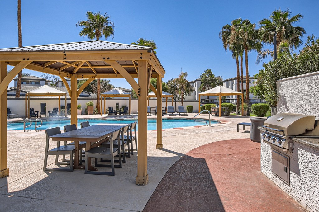 a picnic table and grill next to a pool with palm trees in the background