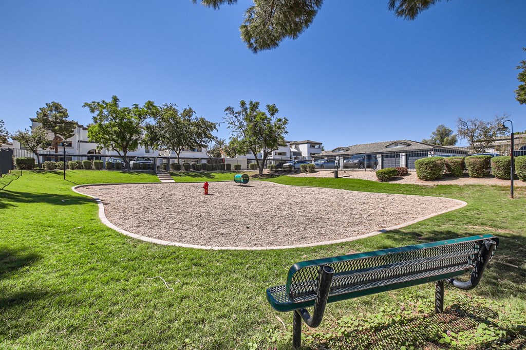 a park bench overlooking a gravel play area with a fire hydrant and trees