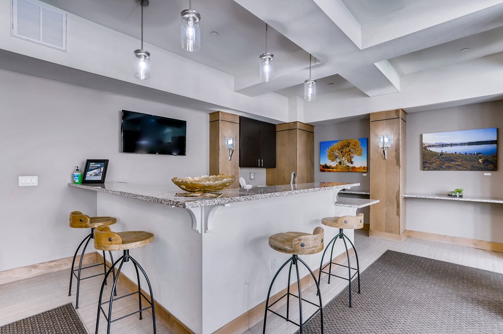 a kitchen with a bar with three stools and a tv on the wall