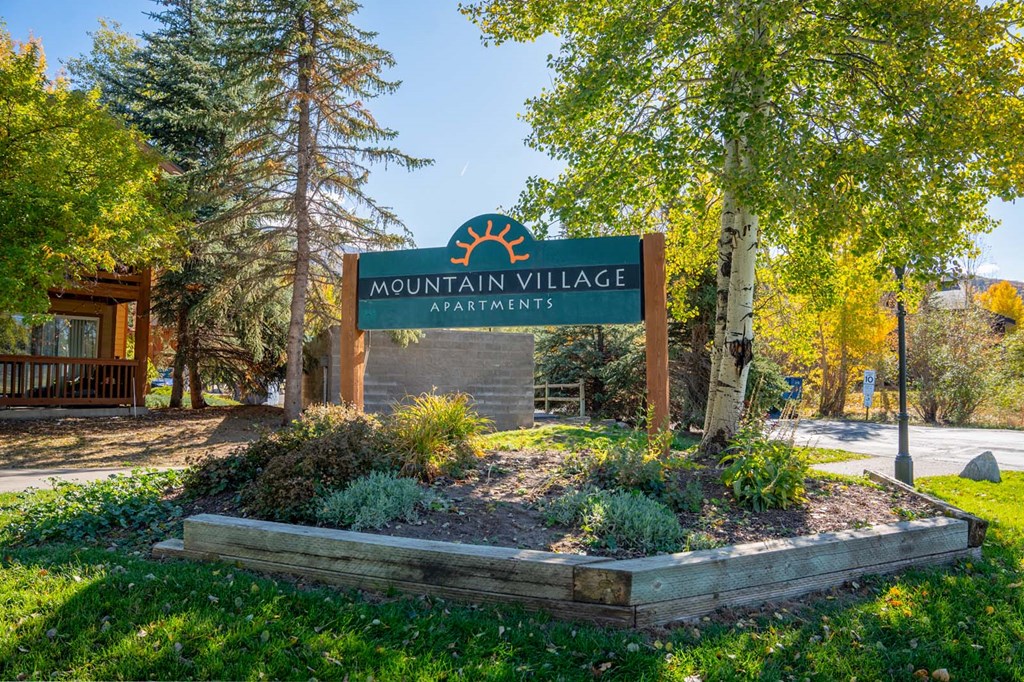 a sign for mountain village apartments in front of trees