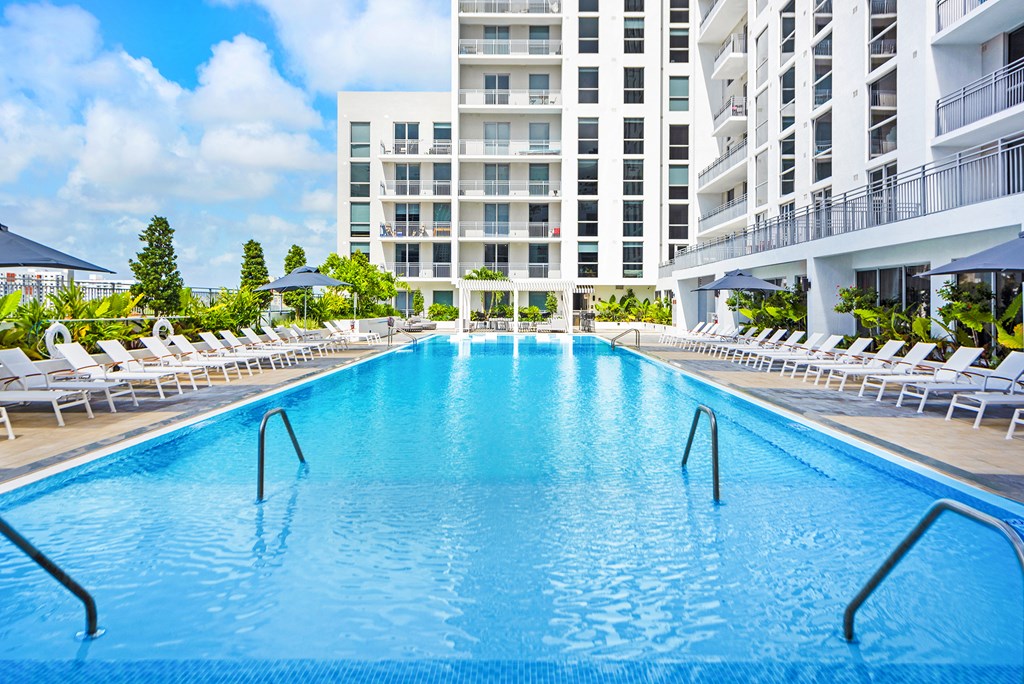 a resort style pool with white chaise lounge chairs and a large white building in the background