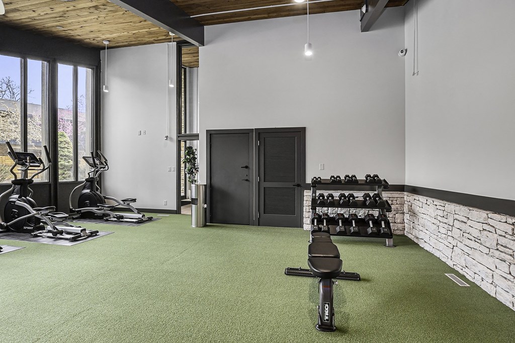 a gym with green carpet and a stone wall with weights and a window