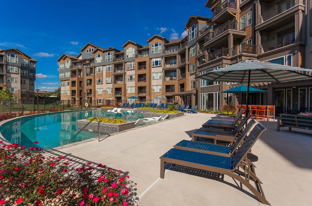 an outdoor pool with lounge chairs and umbrellas next to an apartment building