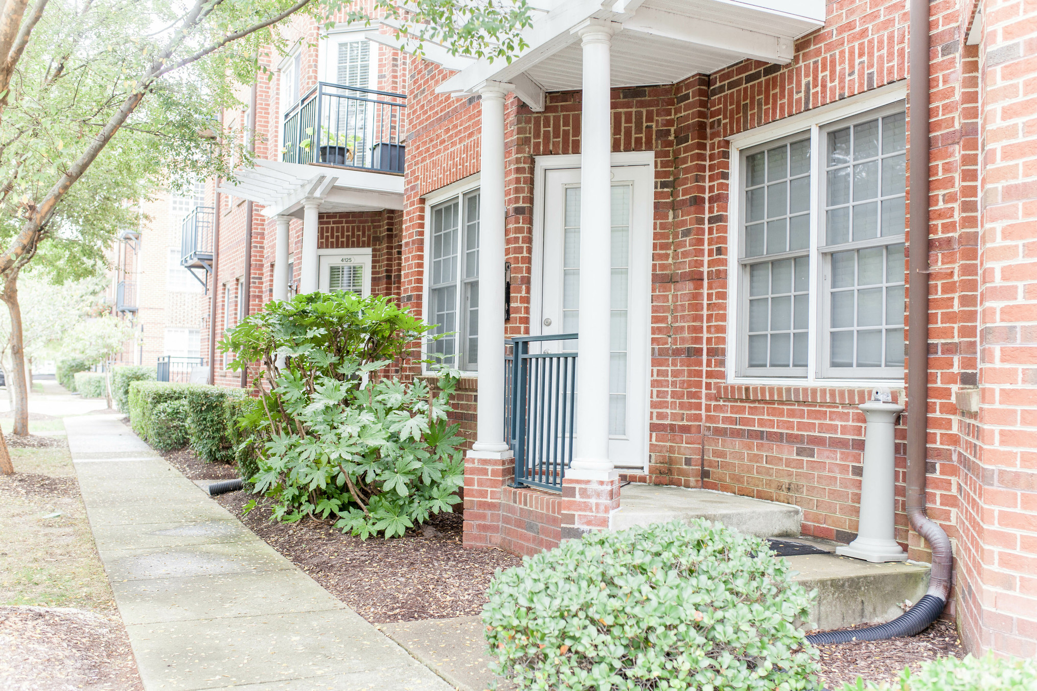 a brick house with white pillars and a sidewalk in front of it