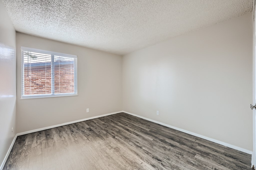 an empty bedroom with wood flooring and a window