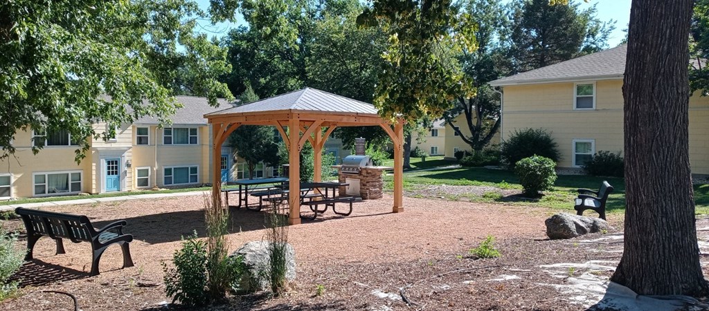 a gazebo with a firepit and benches in front of a yellow apartment building