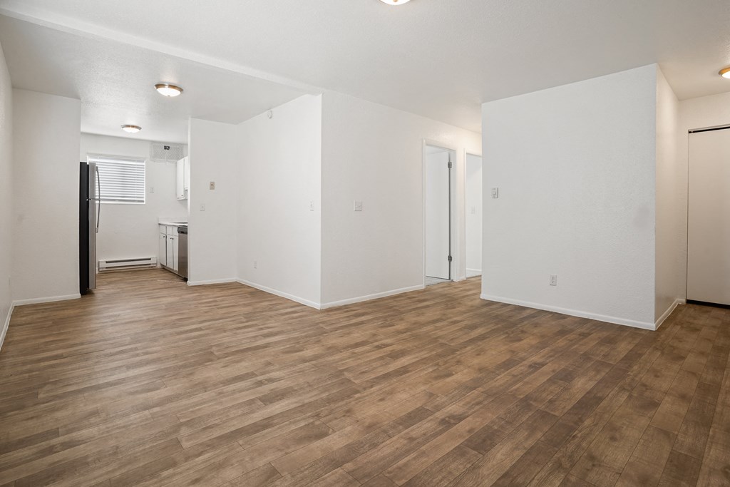 the living room and kitchen of an apartment with white walls and wood flooring