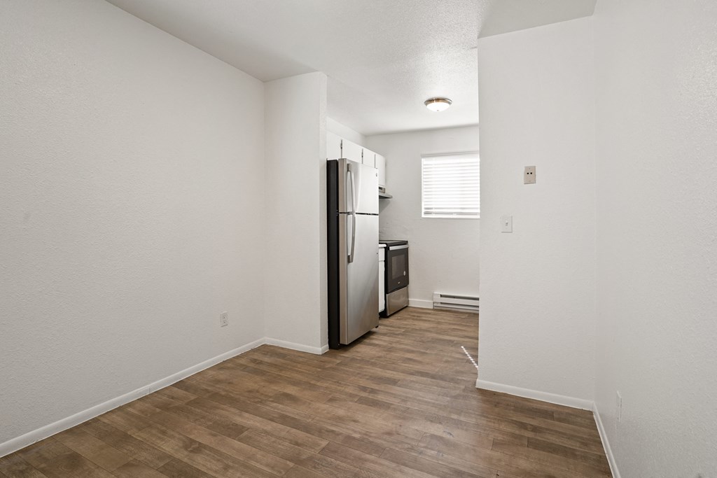 an empty living room with a refrigerator and a kitchen