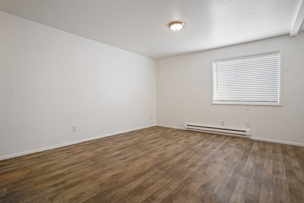 the living room of an apartment with wood flooring and a window