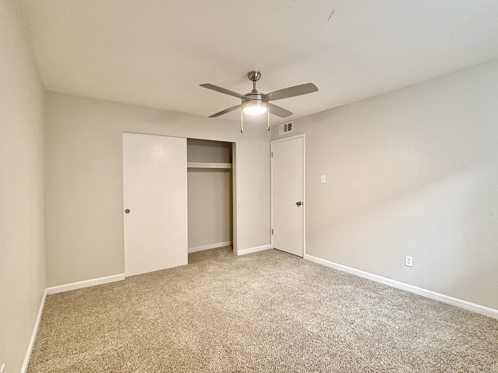 an empty living room with a ceiling fan and a closet