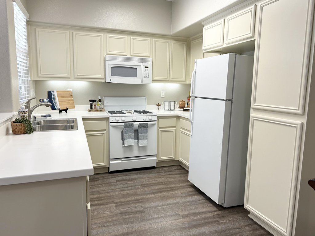 a kitchen with white cabinets and white appliances at Riverton of the High Desert Apartments,Victorville, CA