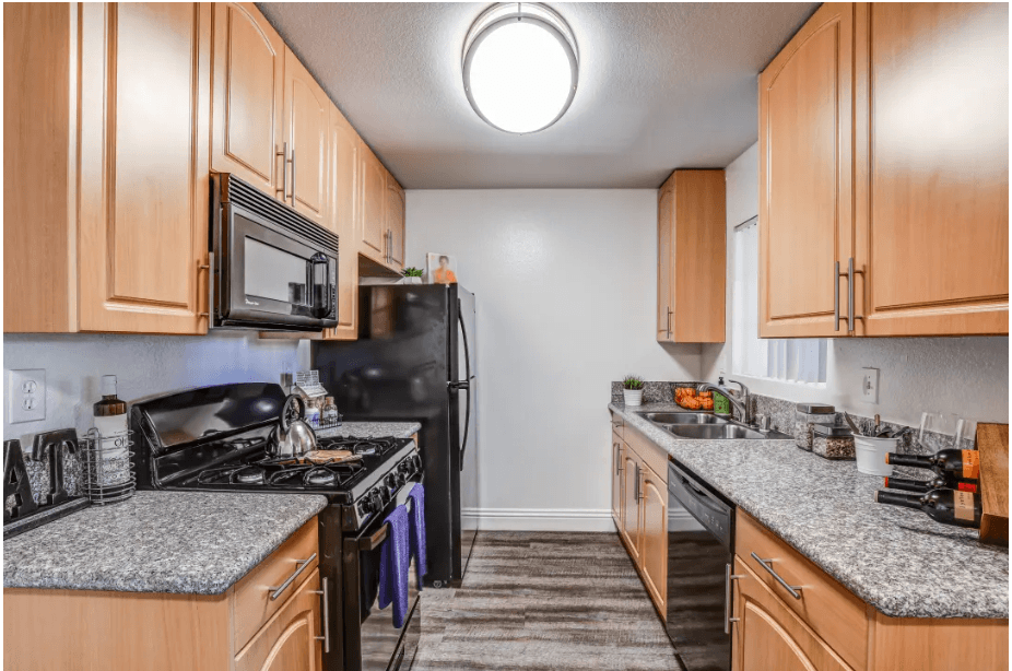 a kitchen with wood cabinets and granite counter tops and black appliances at Vista Promenade Apartments, Temecula, CA