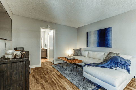 Upland, CA, Apartments Near Ontario Mills - Aspire Upland - Living Room with a White Couch, Wood-Style Flooring, a Door to the Bathroom, and Stylish Decor