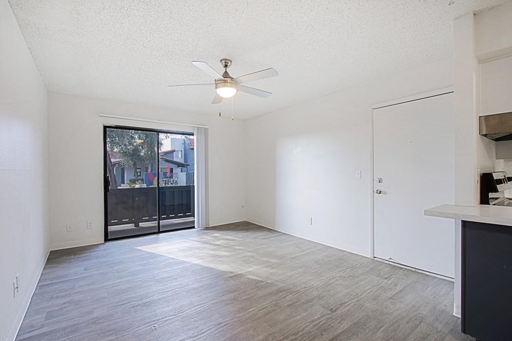 an empty living room with a ceiling fan and a door to a balcony