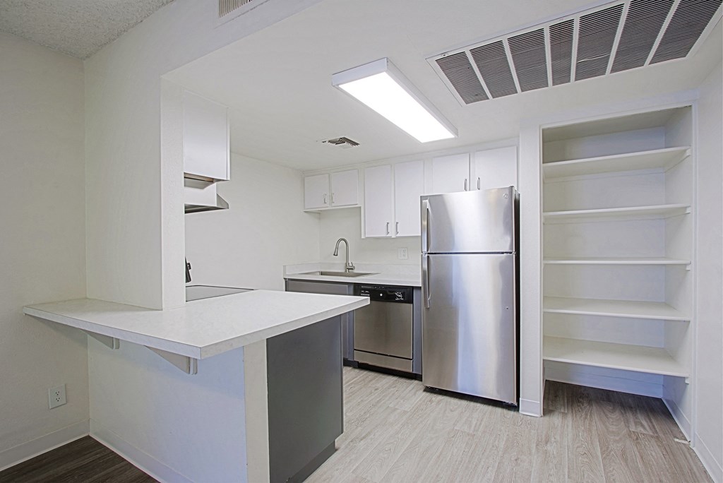 an empty kitchen with a stainless steel refrigerator and white cabinets