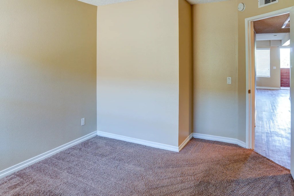 a living room with a carpeted floor and a white wall at The Arches at Regional Center West Apartments, California