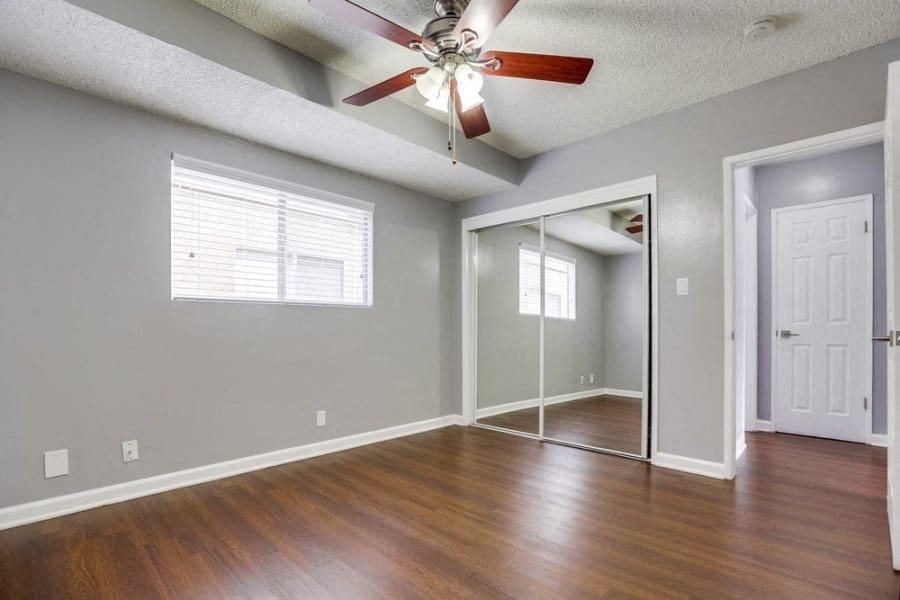Pet-Friendly Apartments in West Covina CA - Tuscany Villas - Bedroom with Wood-Style Flooring, Mirrored Closet Door, and a Ceiling Fan at Tuscany Villas Apartments, West Covina, CA