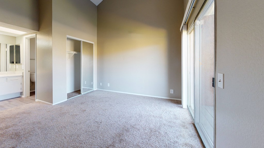 Apartments Ontario CA - Rancho Vista - Unfurnished Bedroom With Connected Bathroom Sink and Counter, Plush Carpet Floors, and Natural Light From the Sliding Glass Door at Rancho Vista Townhomes, Calif